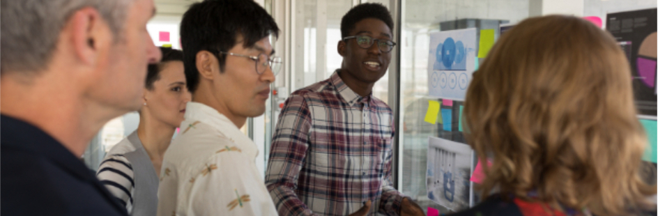 A group of people talk to each other in front of a board with sticky notes.