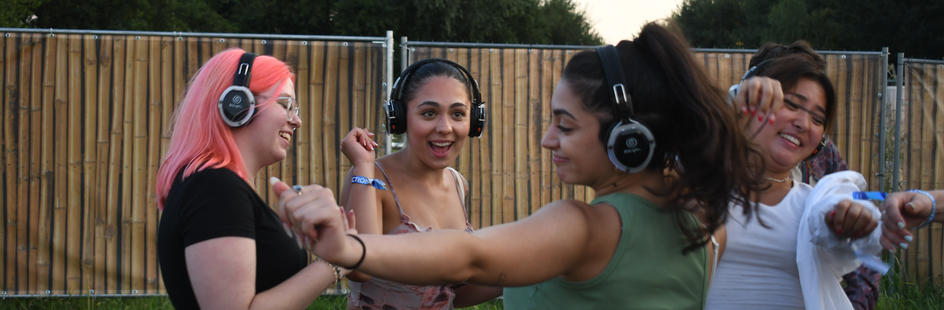 Four young women dance during a silent disco in a garden.