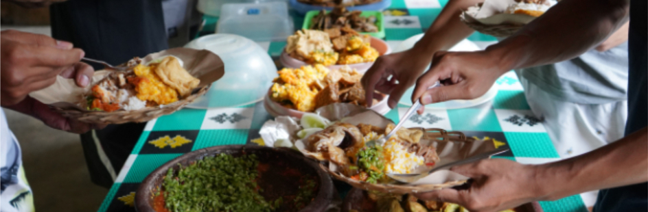 At a long table, people are helping themselves to food.