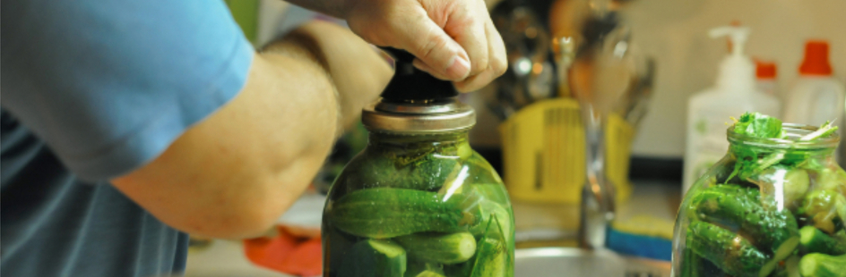 Een man sluit het deksel van een pot met ingelegde augurken.